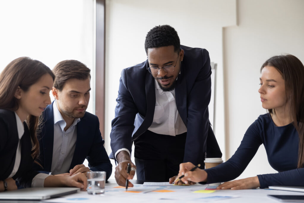 Businessman holds lead meeting with diverse colleagues in office. Businesspeople brainstorm and discuss company financial paperwork at briefing.